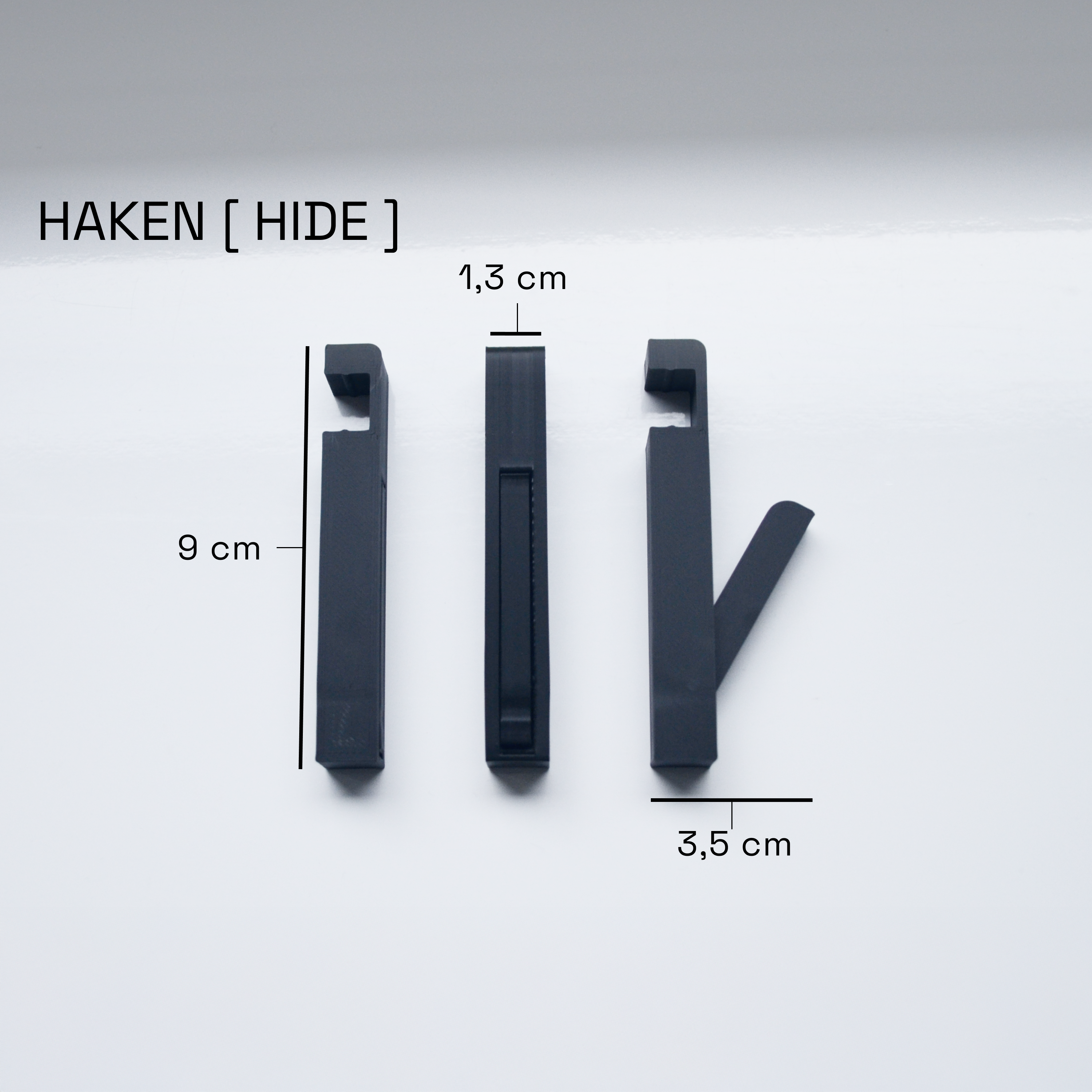 Schwarze klapphaken "HIDE" in drei Ansichten mit den Maßen 9 cm x 1,3 cm x 3,5 cm auf weißem Hintergrund. Hochwertiges Akustikpaneel zubehör für moderne Wandpaneele und stilvolle Garderoben. Perfekt für eine bohrfreie Montage in Flur, Eingangsbereich oder Schlafzimmer.