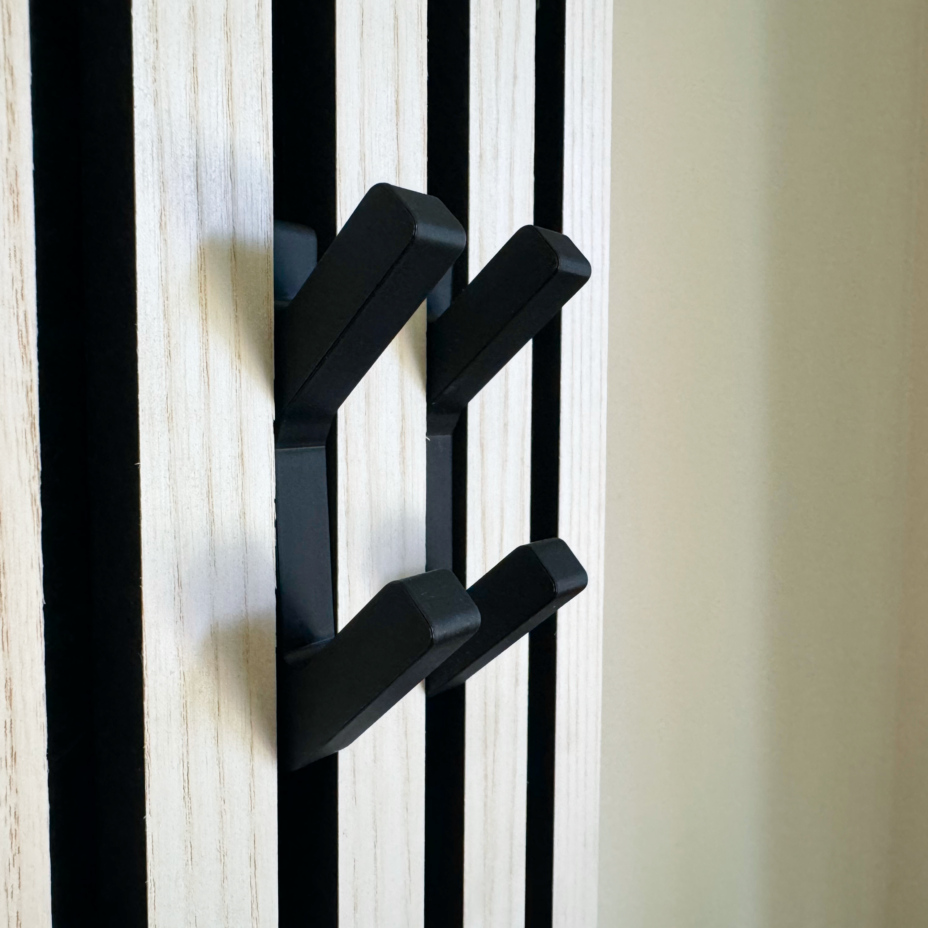 Stabile, schwarze Doppelhaken auf stilvollen Wandpaneelen in Holzoptik – perfekt als Akustikpannel Zubehör. Die moderne Hakenlösung eignet sich ideal für Garderoben, da sie ohne Bohren direkt in Akustikpaneele eingesetzt wird. So entsteht ein funktionales und ästhetisches Design-Element, das sowohl in Wohnräumen als auch im Eingangsbereich ein echter Blickfang ist.