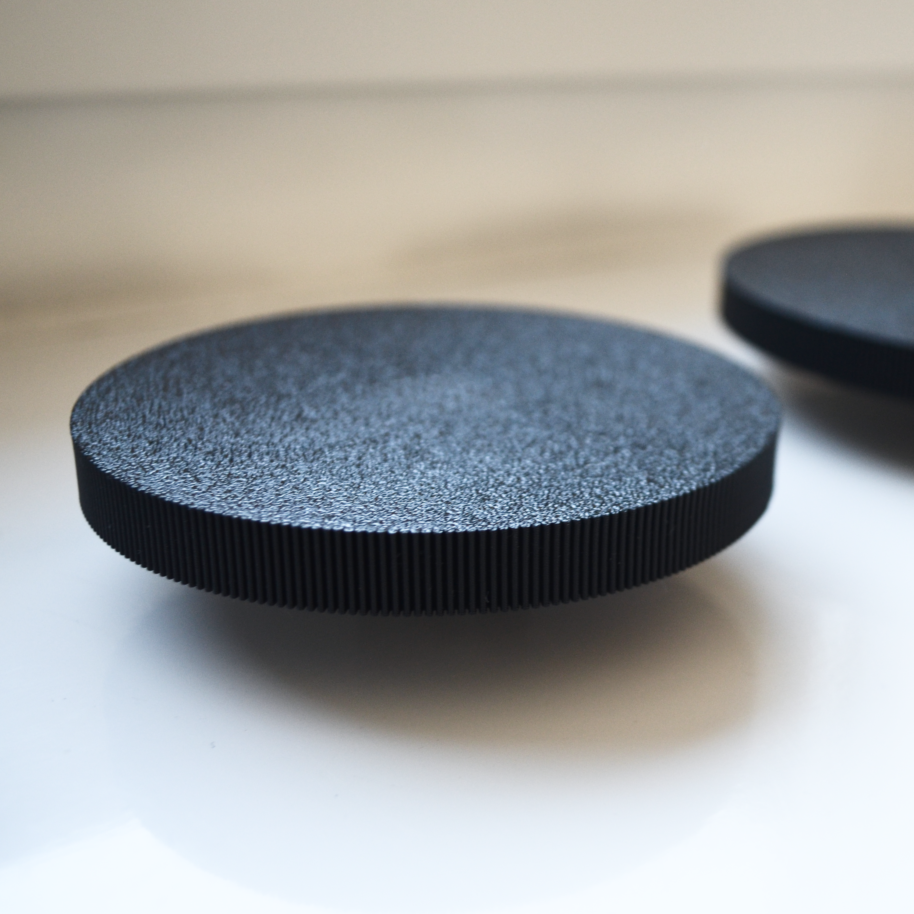 Schwarzer, runder Wandhaken mit strukturierter Oberfläche und geriffeltem Rand in Nahaufnahme. Hochwertiges Akustikpaneel-Zubehör für moderne Wandpaneele und stilvolle Garderoben. Ideal für eine bohrfreie Montage in Flur, Eingangsbereich oder Schlafzimmer.