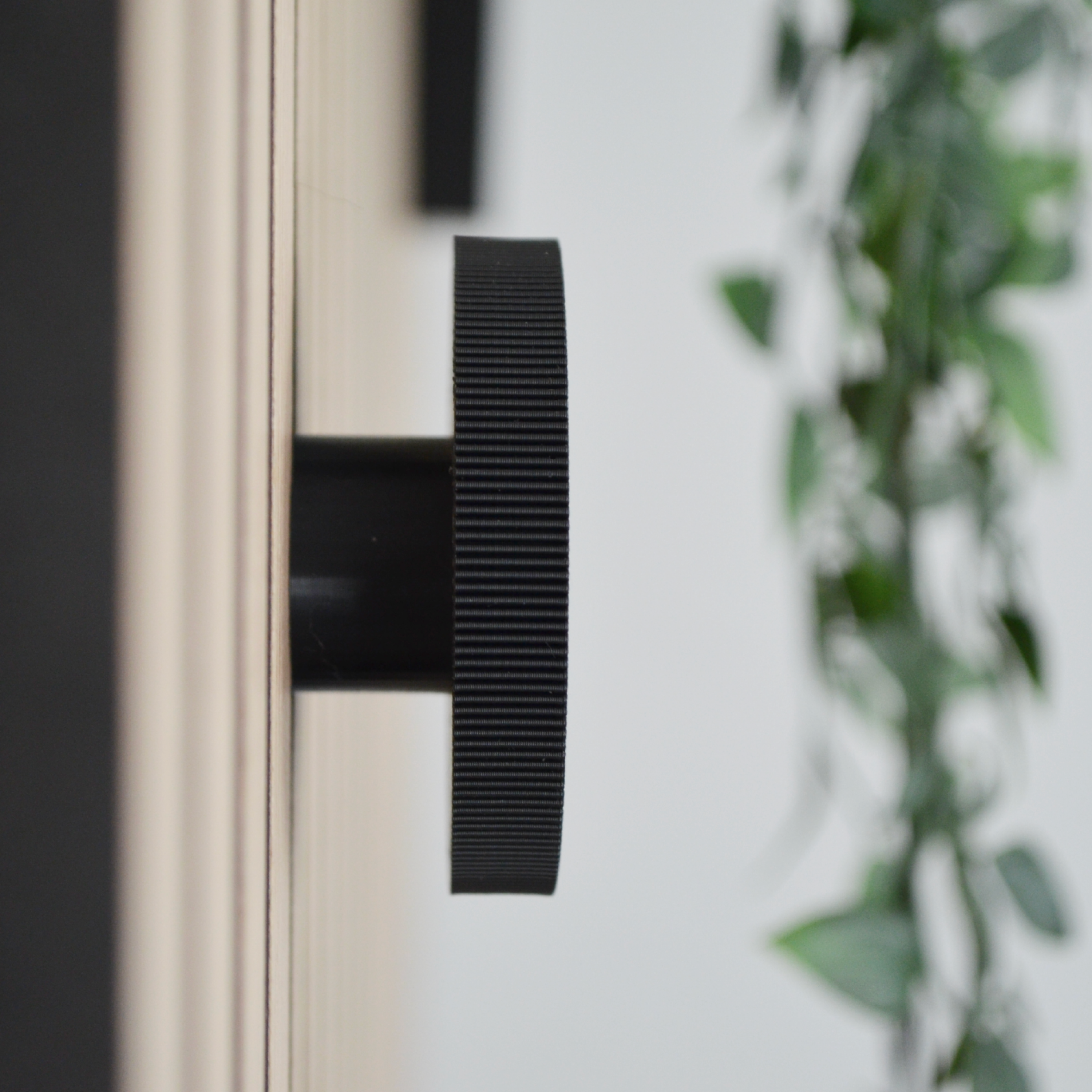 Seitliche Nahaufnahme eines schwarzen, geriffelten Wandhakens, montiert an einem modernen Wandpaneel. Hochwertiges Akustikpaneel Zubehör für stilvolle Garderoben. Die bohrfreie Montage sorgt für eine einfache Installation in Flur, Eingangsbereich oder Schlafzimmer.